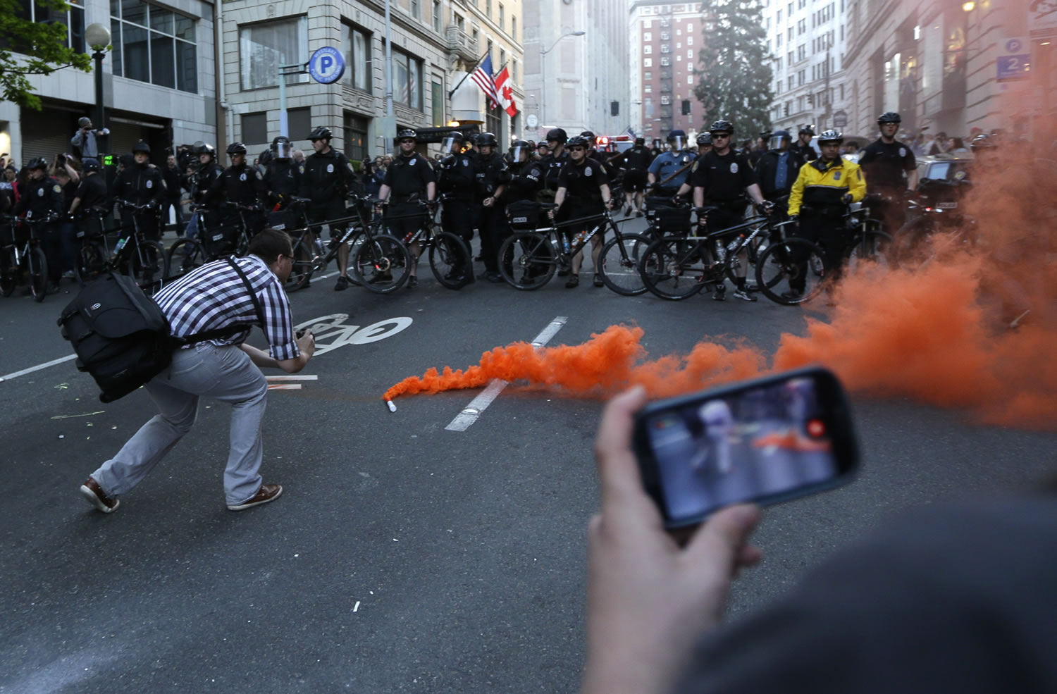A man uses a mobile phone to photograph a man photographing a smoke device dropped in front of a row of Seattle Police officers during a May Day march that began as an anti-capitalism protest and turned into demonstrators clashing with police Wednesday in downtown Seattle.