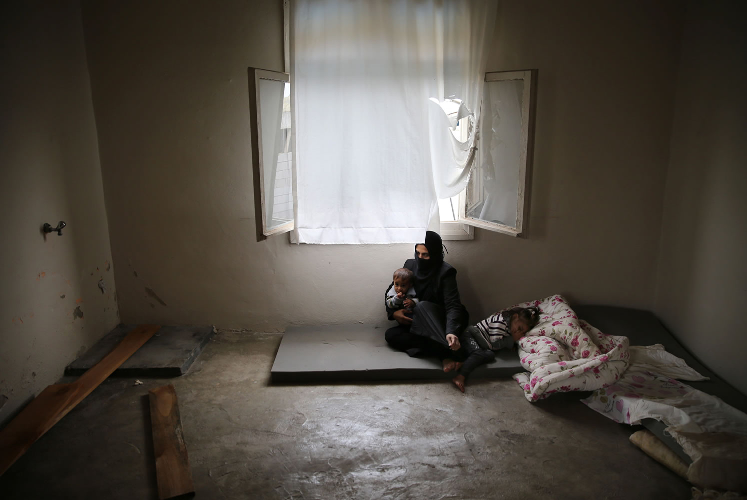 Syrian refugee Hind Salem, who fled with her family from the central Syrian town of Palmyra, from Russian airstrikes, sits on the ground with her kids at their unfurnished home, in the Turkish-Syrian border city of Reyhanli, southern Turkey.