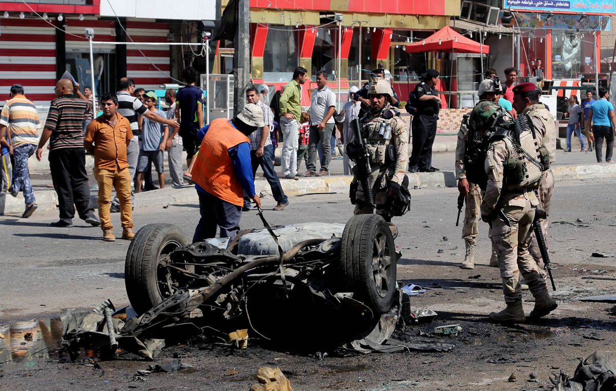 A Baghdad municipality worker cleans while people and security forces inspect the site of a car bomb attack in Sadr City, Baghdad, Iraq, on Wednesday.