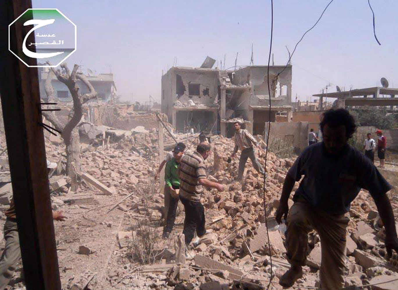 In this citizen journalism image provided by Qusair Lens, which has been authenticated based on its contents and other AP reporting, Syrians inspect the rubble of damaged buildings due to government airstrikes Saturday in Qusair, Homs province, Syria.