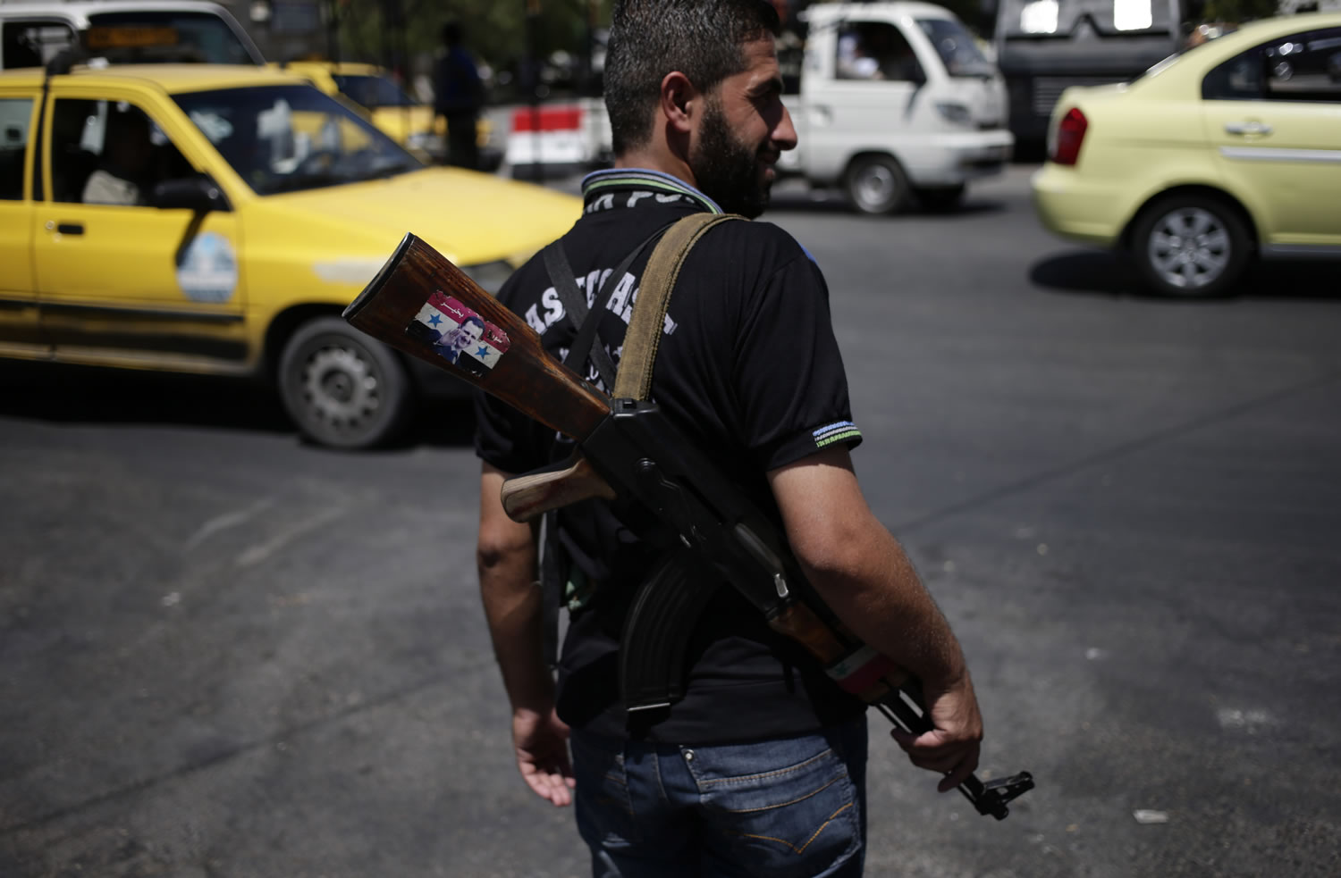 A Syrian military soldier holds his Ak-47 with a sticker of Syrian President Bashar Assad and Arabic that reads, &quot;Syria is fine,&quot; as he stands guard at a check point on Baghdad street, in Damascus, Syria, on Wednesday.