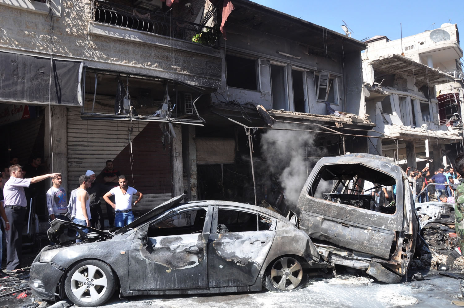 Syrian citizens gather near damaged cars that were burned after a car bomb exploded in the suburb of Jaramana, Damascus, Syria, on Thursday.