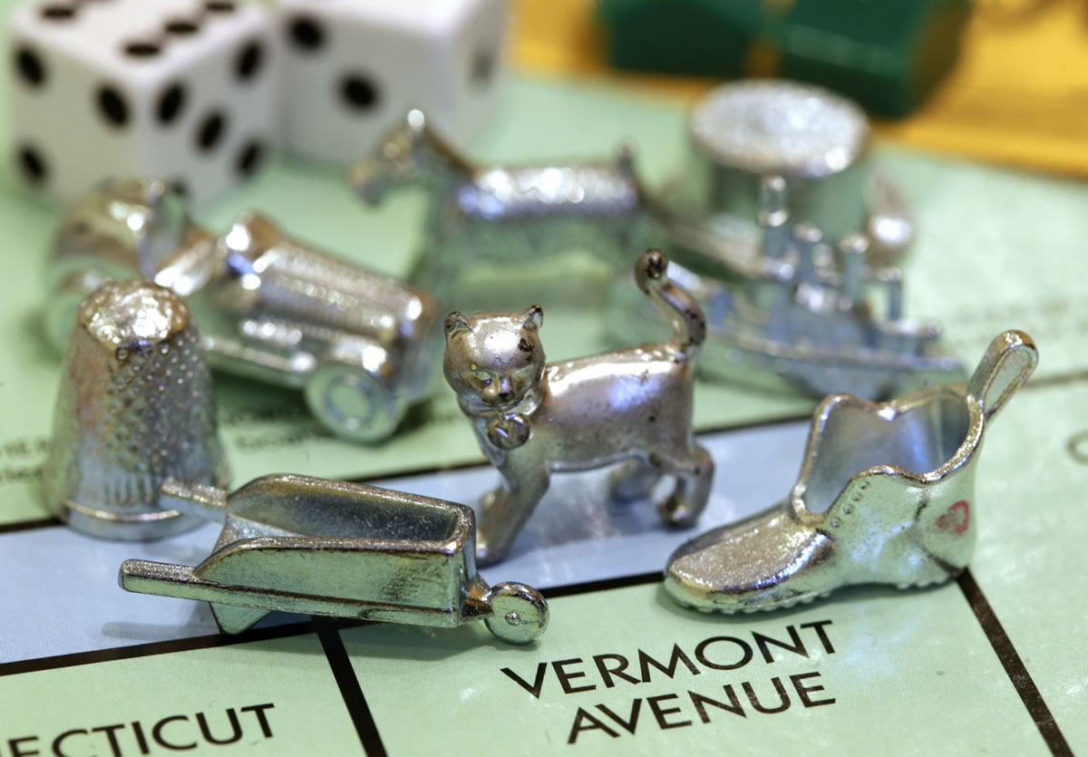 The newest Monopoly token, a cat, center, rests on a Boardwalk deed next to other tokens still in use including the wheelbarrow, left, and the shoe, right.