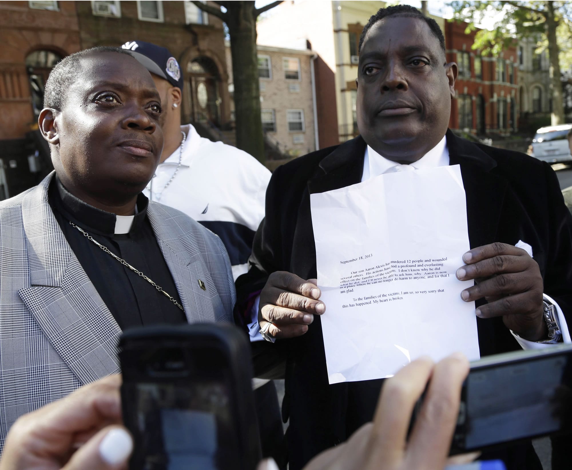 While reporters take pictures, Bishop Gerald Seabrooks, right, holds up a copy of a statement made by Cathleen Alexis, mother of suspected Navy Yard shooter Aaron Alexis, as Bishop Willie Billips looks on in Brooklyn, N.Y., on Wednesday