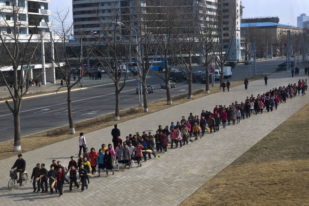 North Korean children carrying brooms walk on a sidewalk in Pyongyang on Wednesday on their way to help tidy up the area around bronze statues of the late leaders as the capital city prepares to mark the April 15 birthday of its founder Kim Il Sung.