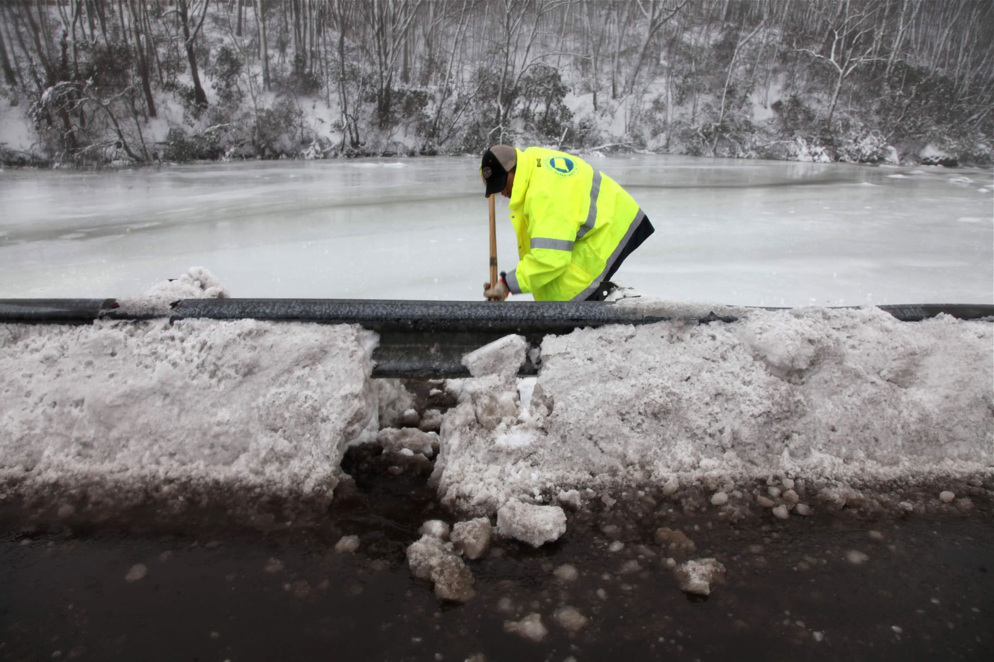 A state worker punches a hole in a snow berm Monday so standing water can drain off a bridge in East Lyme, Conn.