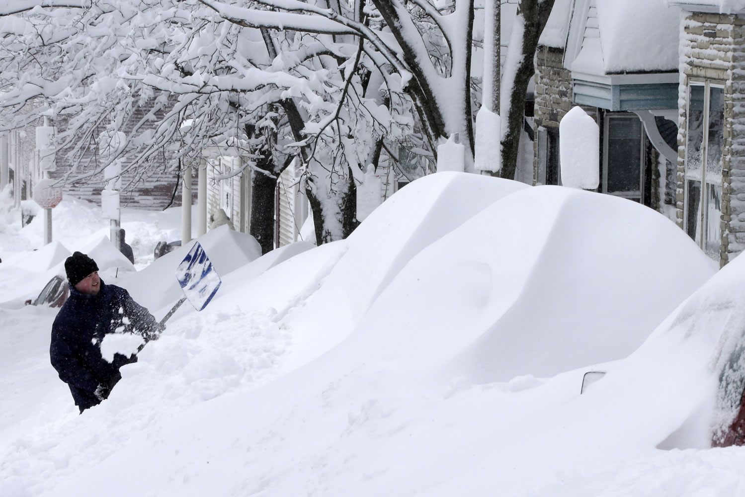 A man shovels snow off his car in front of his home on Saturday in Boston.