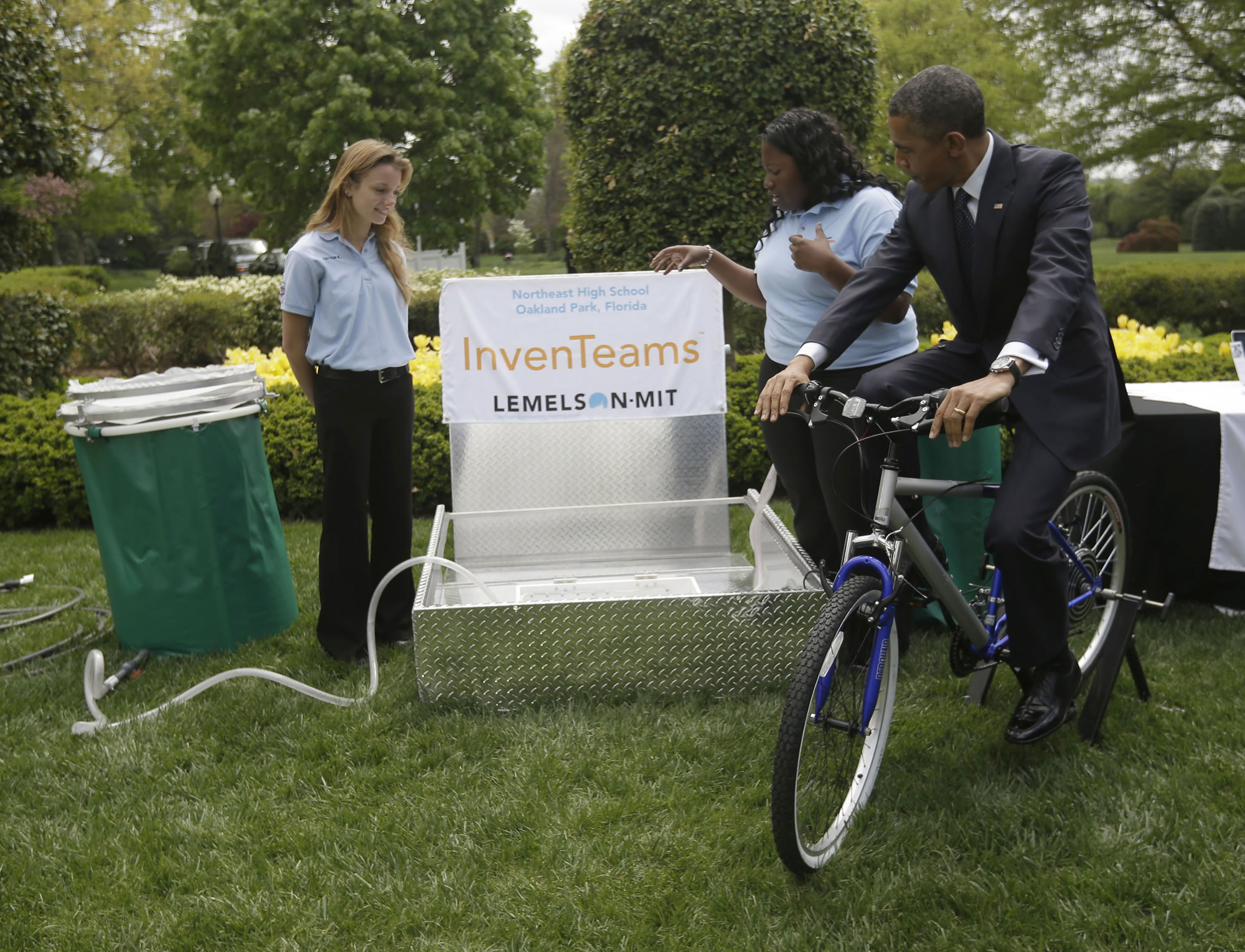 President Barack Obama pedals a bicycle-powered emergency water-sanitation station as Payton Karr, 16, left, and Kiona Elliott, 18, look on.