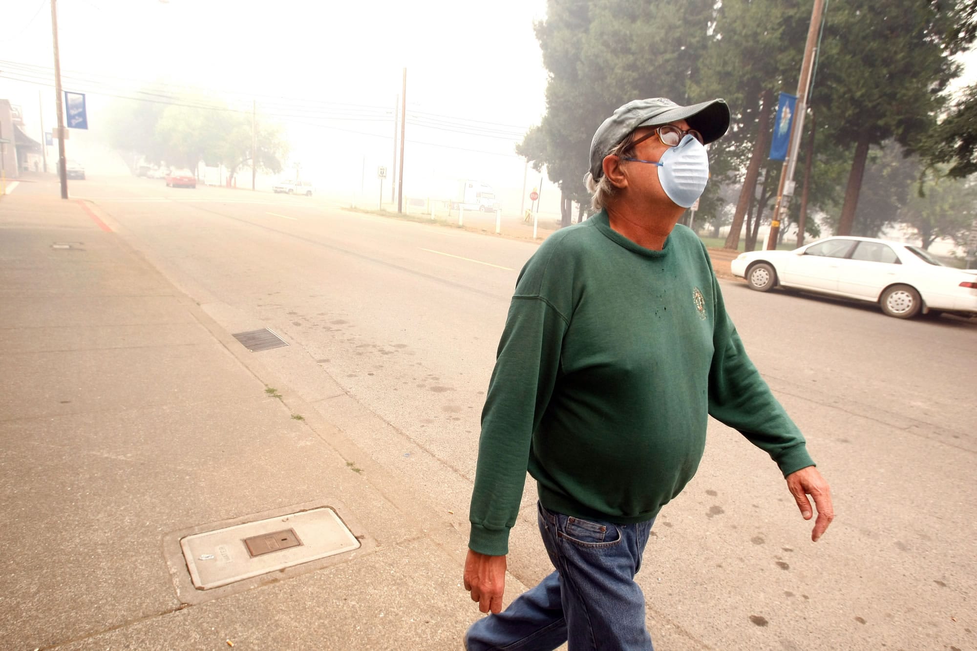Jim Crouch wears a mask as he walks to the post office in Glendale, Ore., on Tuesday. Lightning late last week touched off dozens of fires in southwest Oregon near Glendale.