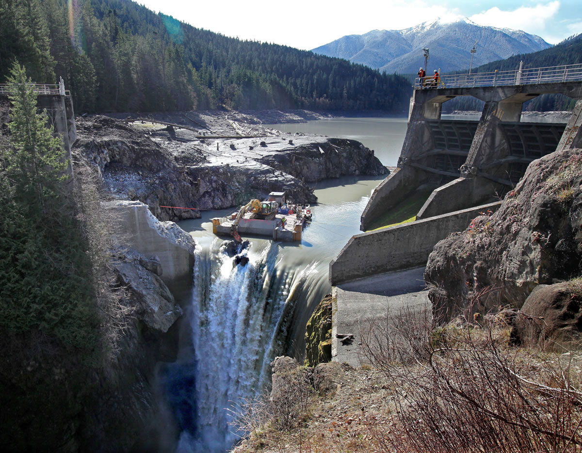 An excavator on a barge chips away March 19 at the Glines Canyon Dam, 13 miles from the mouth of the Elwha River near Port Angeles; the demolition should be finished by May.