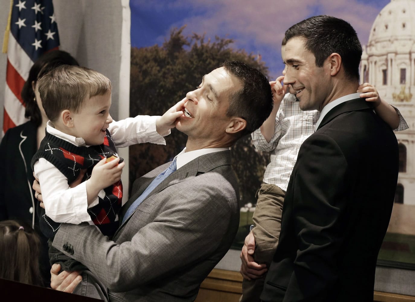 Dr. Paul Melchert, left, gets interrupted by son, Emmett, as he attempts to address the media while his partner, James Zimerman, right, holds twin Gabriel during a news conference in St.