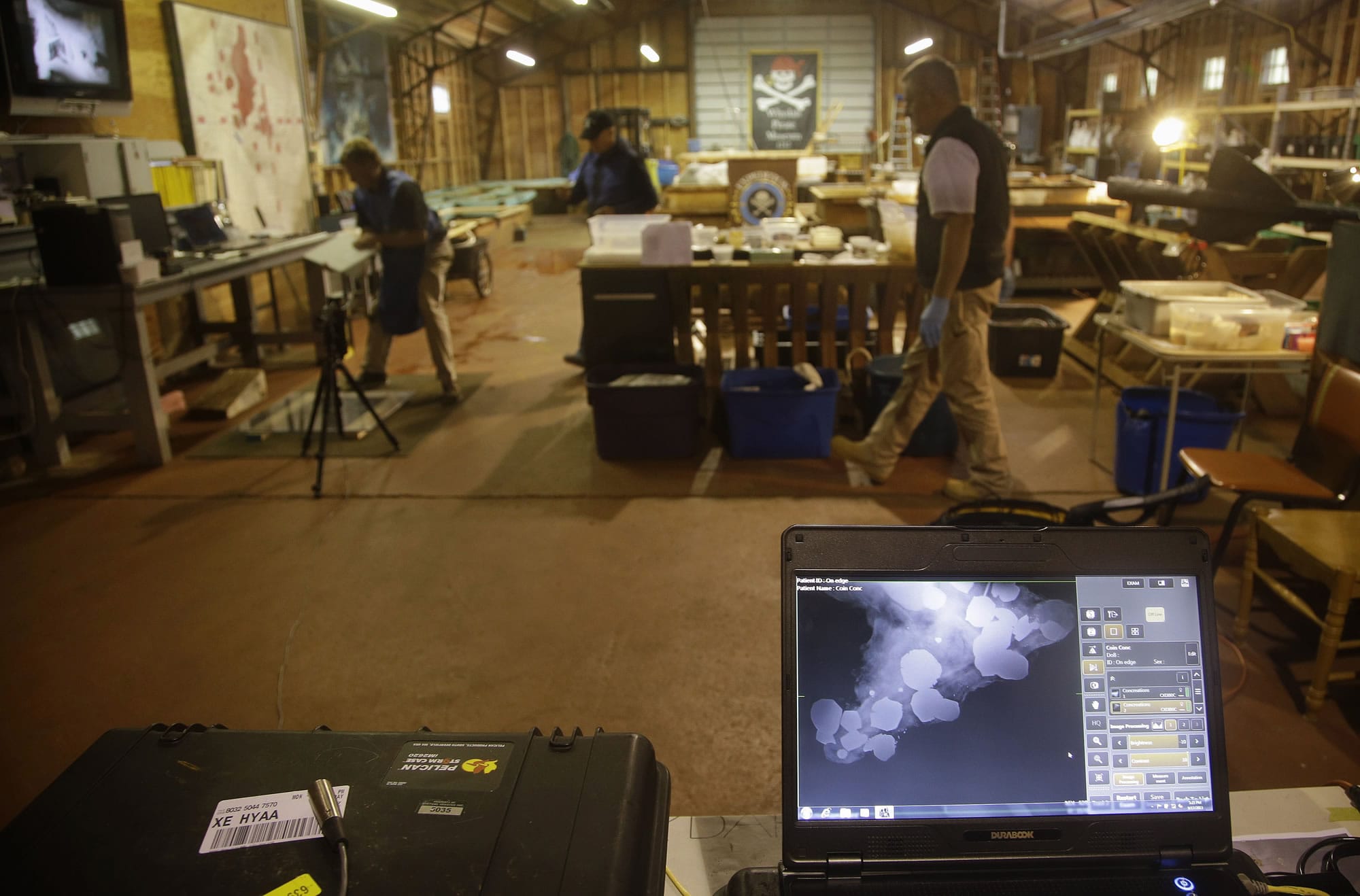 An X-ray of a concretion, front, a rocky mass that forms when metals such as gold and silver chemically react to salt water, is seen on a laptop computer at the Whydah pirate ship museum's warehouse in Brewster, Mass., on Tuesday.