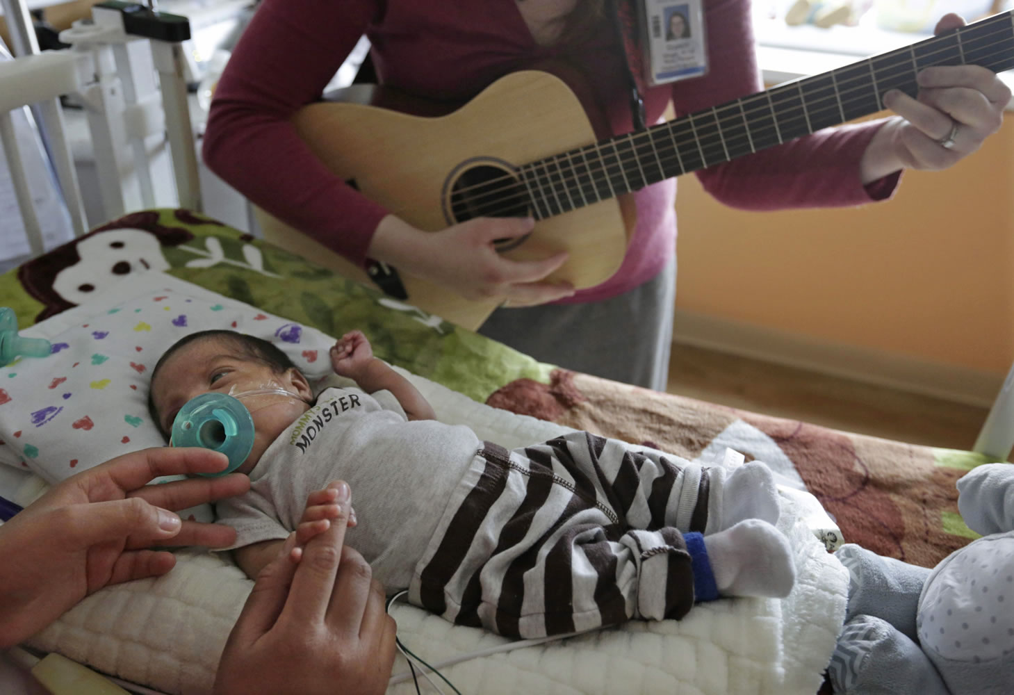 Music therapist Elizabeth Klinger, right, quietly plays guitar and sings for Augustin as he grips the hand of his mother, Lucy Morales, in the newborn intensive care unit at Ann &amp; Robert H. Lurie Children's Hospital in Chicago on May 6. Research suggests that music may help those born way too soon adapt to life outside the womb.