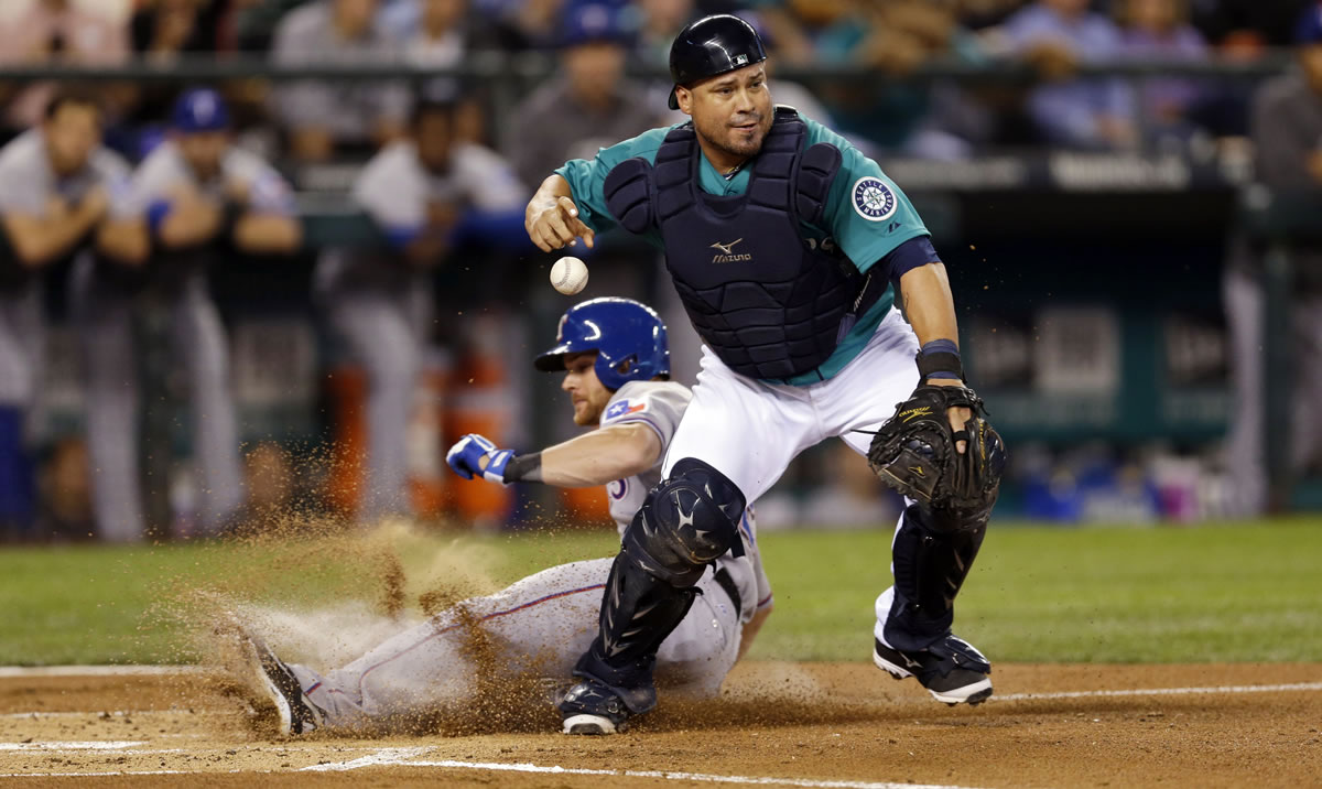 Seattle Mariners catcher Humberto Quintero loses control of the ball after forcing out Texas Rangers' Craig Gentry, left, at home in the first inning Monday in Seattle.