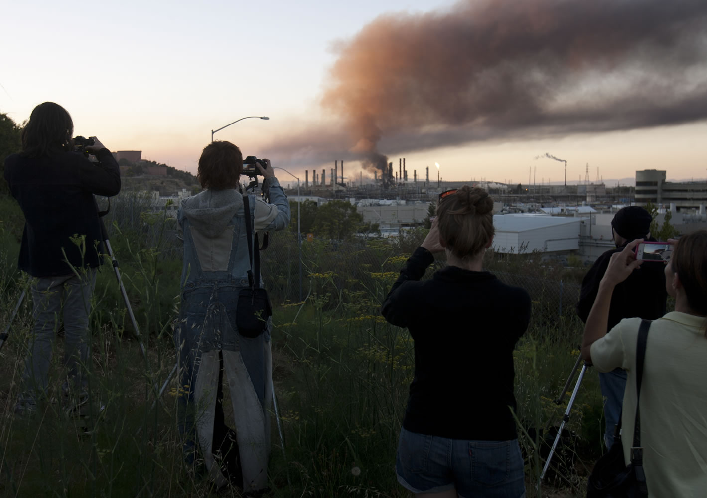 The curious gather on a hillside in Point Richmond, Calif.,  to photograph the the fire in an oil unit at the Chevron refinery in Richmond, Calif., Aug.