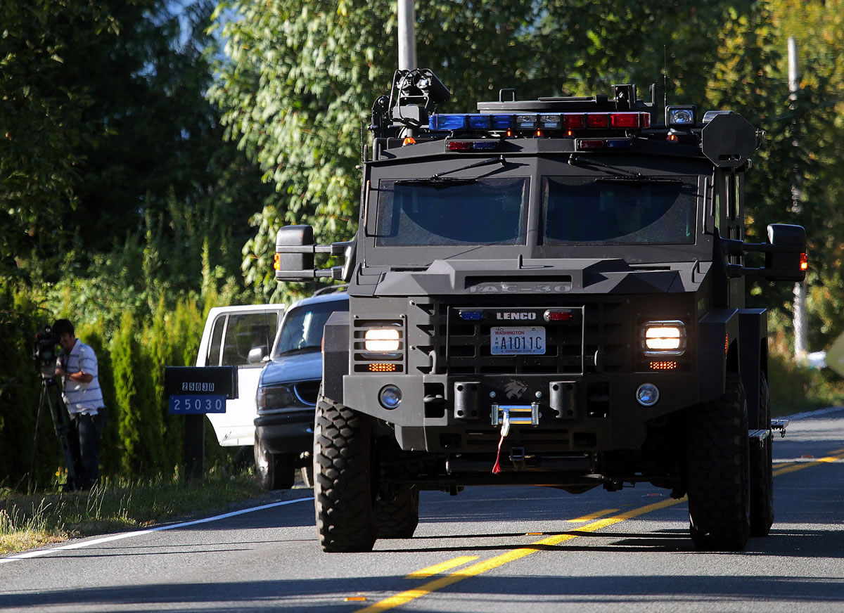 An armored law enforcement vehicle approaches a roadblock at the site where a sniper shot a man and then later opened fire on a SWAT team Sunday near Arlington.