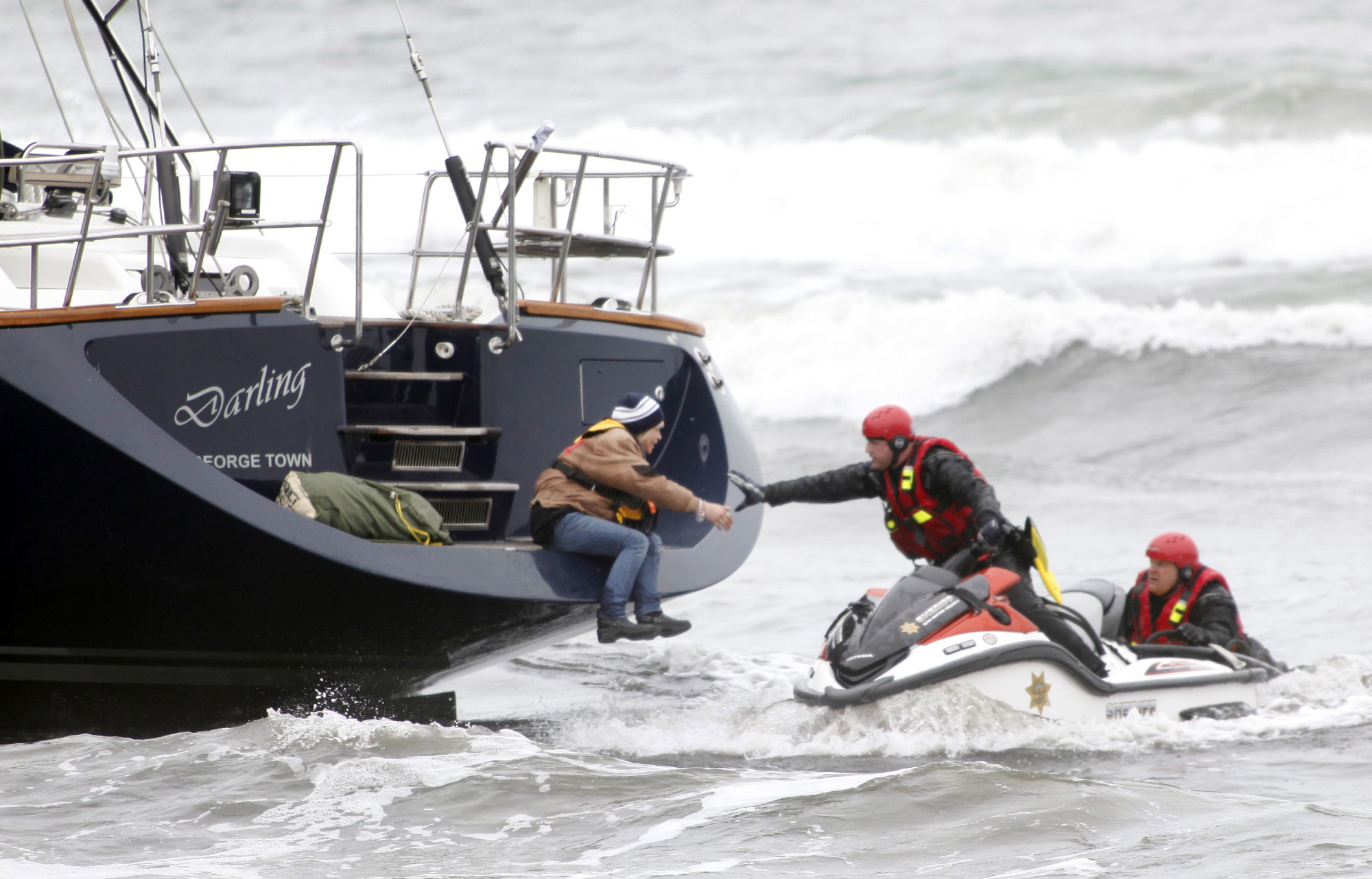 Rescuers attempt to grab a woman off the back of the 82-foot-long sailboat, the Darling, stuck in the surf off Pacifica, Calif., on Monday. Three people were arrested Monday after they stocked a stolen yacht with pizza and beer, and then ran the vessel aground on a Northern California beach, authorities said.