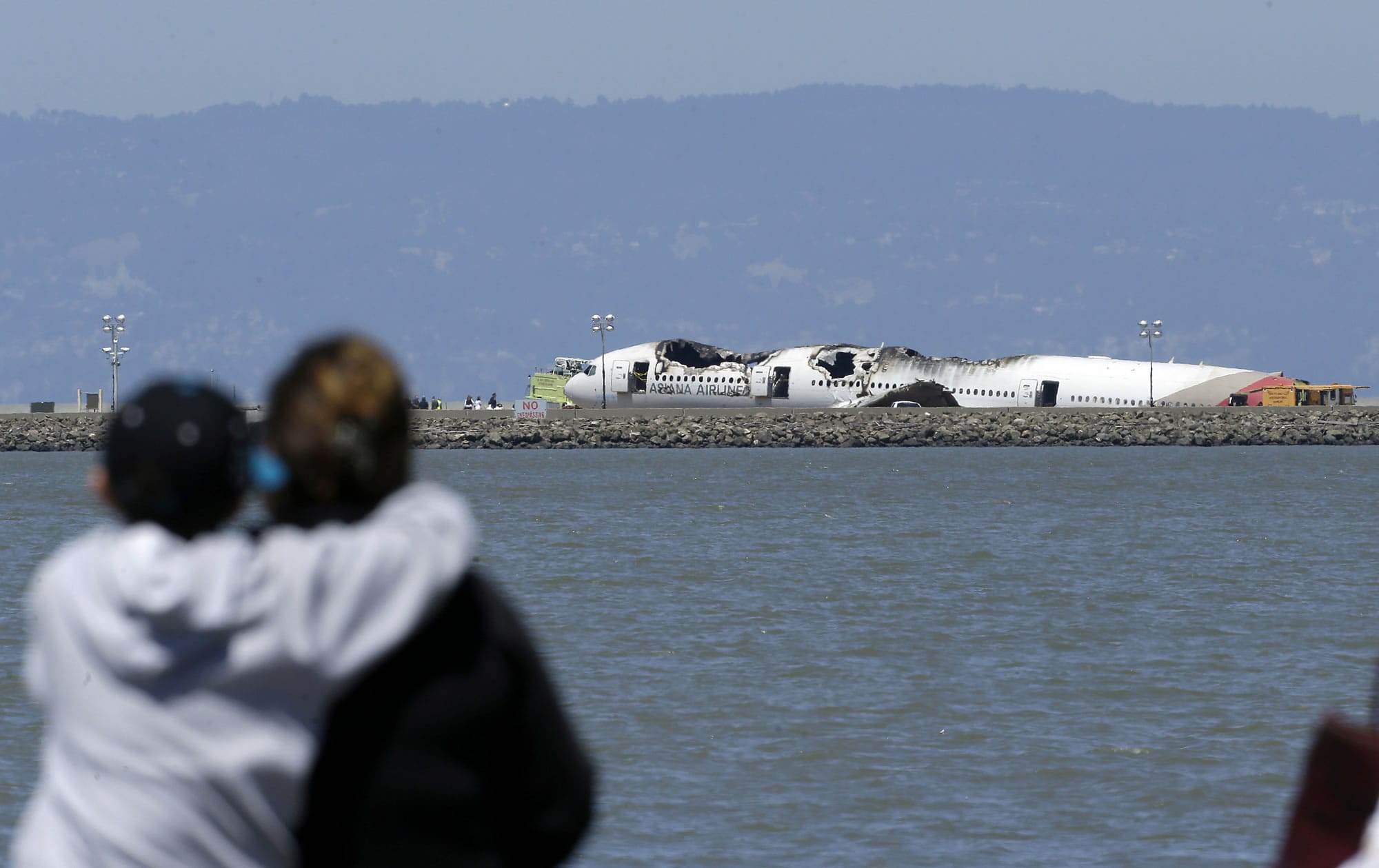 Spectators on Monday look toward the wreckage of the  Asiana Airlines Flight 214 that crashed upon landing Saturday at San Francisco International Airport.