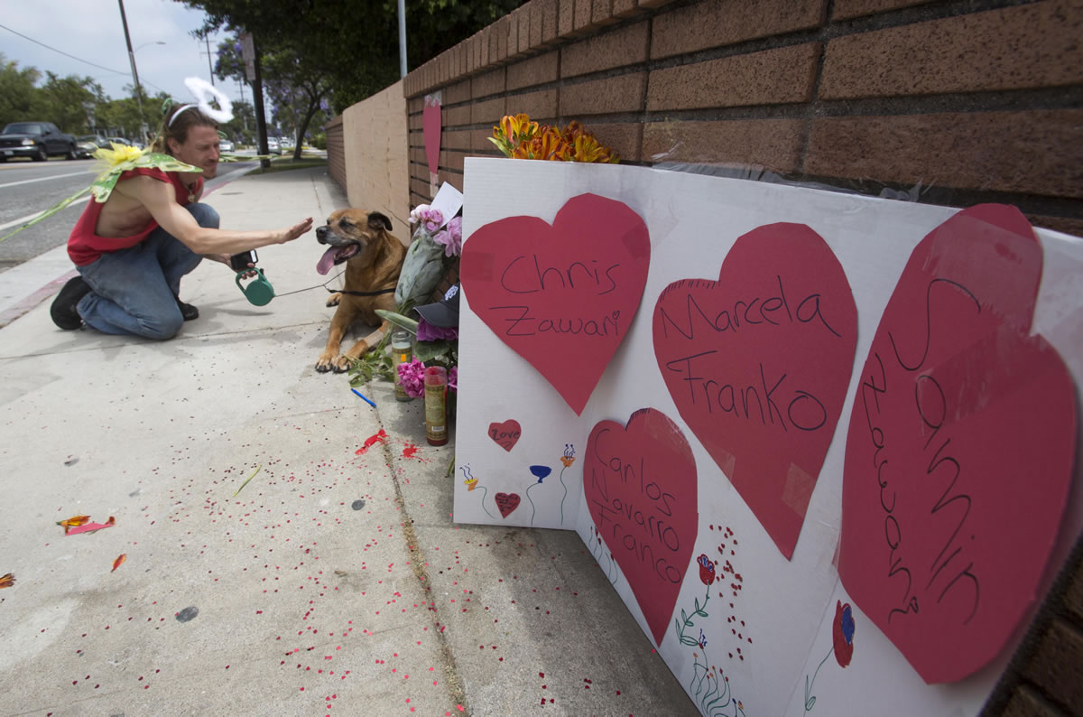 Hearts with messages placed by Nate Edelson, 39, a former student of Santa Monica College, dressed as a Fairly Angel, pets his dog Bull after putting heart-covered messages  at a makeshift memorial Sunday at Santa Monica College, in Santa Monica, Calif.