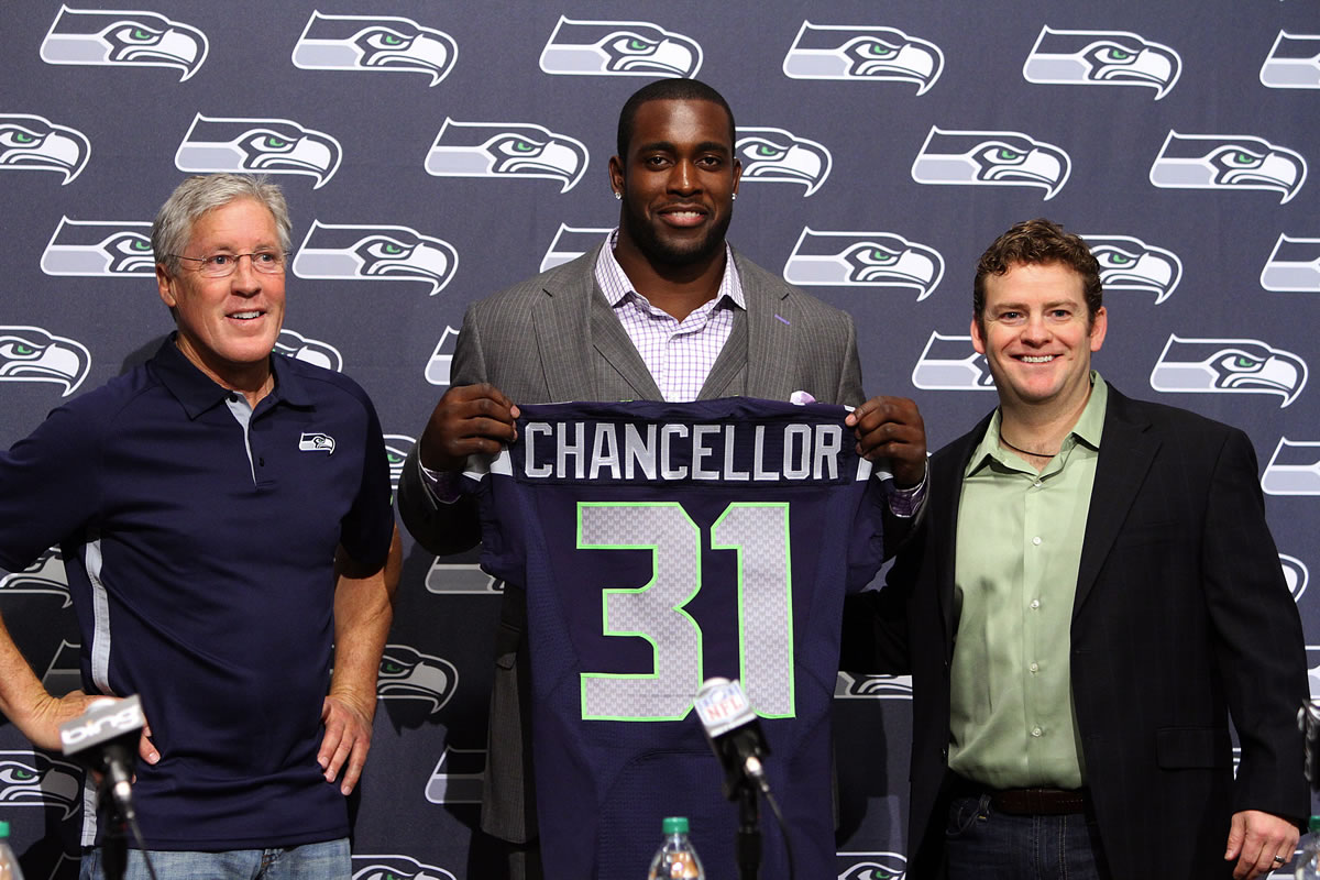 Seattle Seahawks head coach Pete Carroll, left, and general manager John Schneider, far right, pose for photos after announcing a four-year extension to the contract of safety Kam Chancellor, middle, during an NFL football news conference on Monday, April 22, 2013, in Renton, Wash.