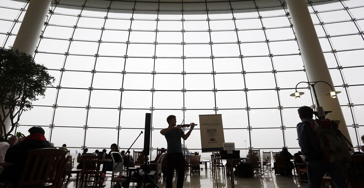 Classical violinist Daniel Butman plays against a backdrop of a multi-story window socked-in with fog in the central terminal at Seattle-Tacoma International Airport Tuesday in SeaTac.