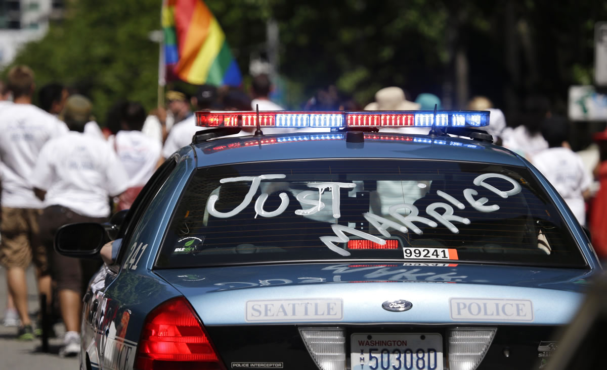 A Seattle Police Deptartment car driven by officer Bob Peth and carrying his husband Aaron Fletcher in the passenger seat proceeds on the route at the annual Gay Pride parade Sunday, June 30, 2013, in Seattle. The couple were married Dec. 9, the first day that same-sex weddings became legal in Washington state.