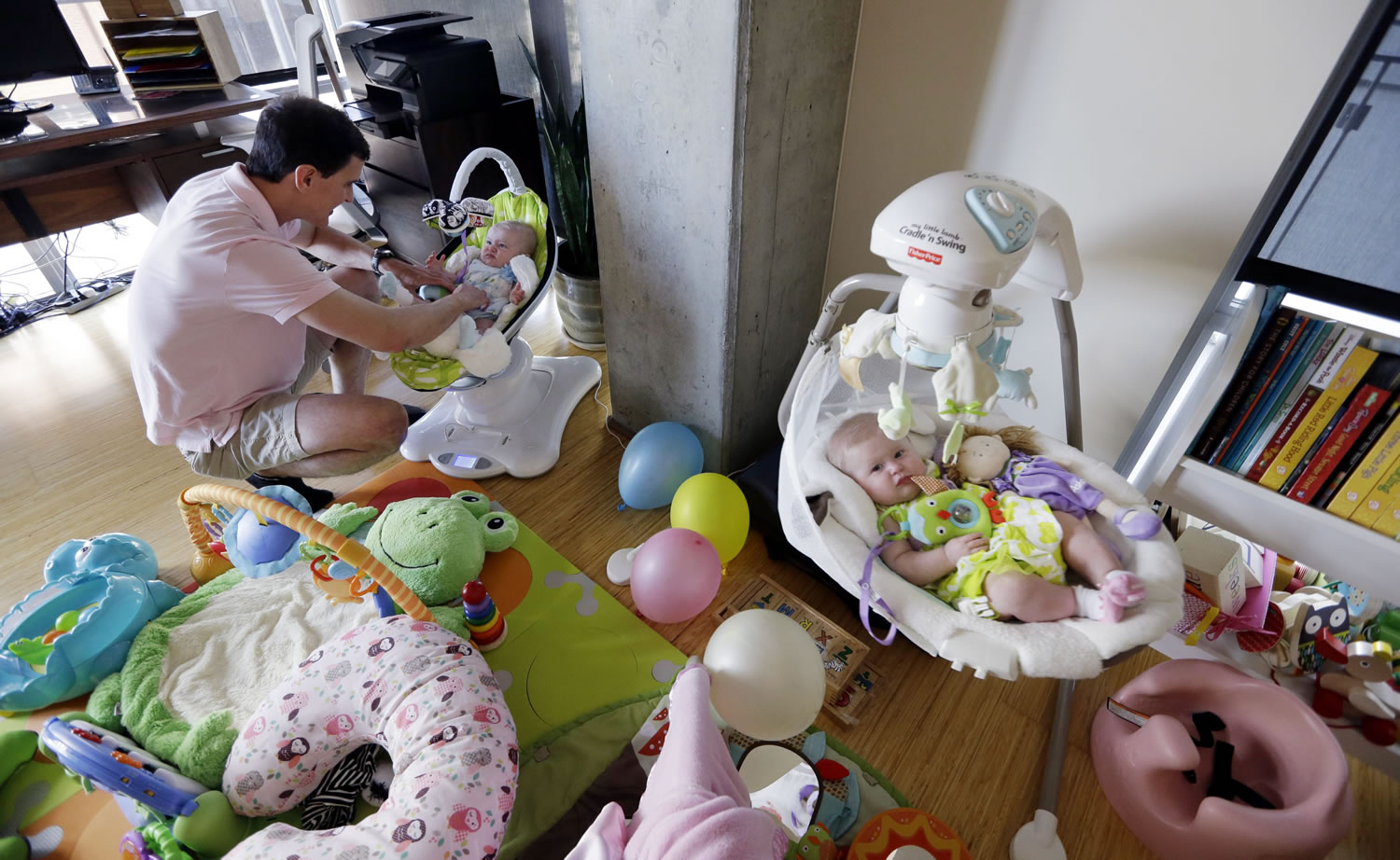 Trey Powell settles his 6-month-old daughter, Kylan, down for a nap as her twin sister, Ashton, lies nearby in their home in Seattle.
