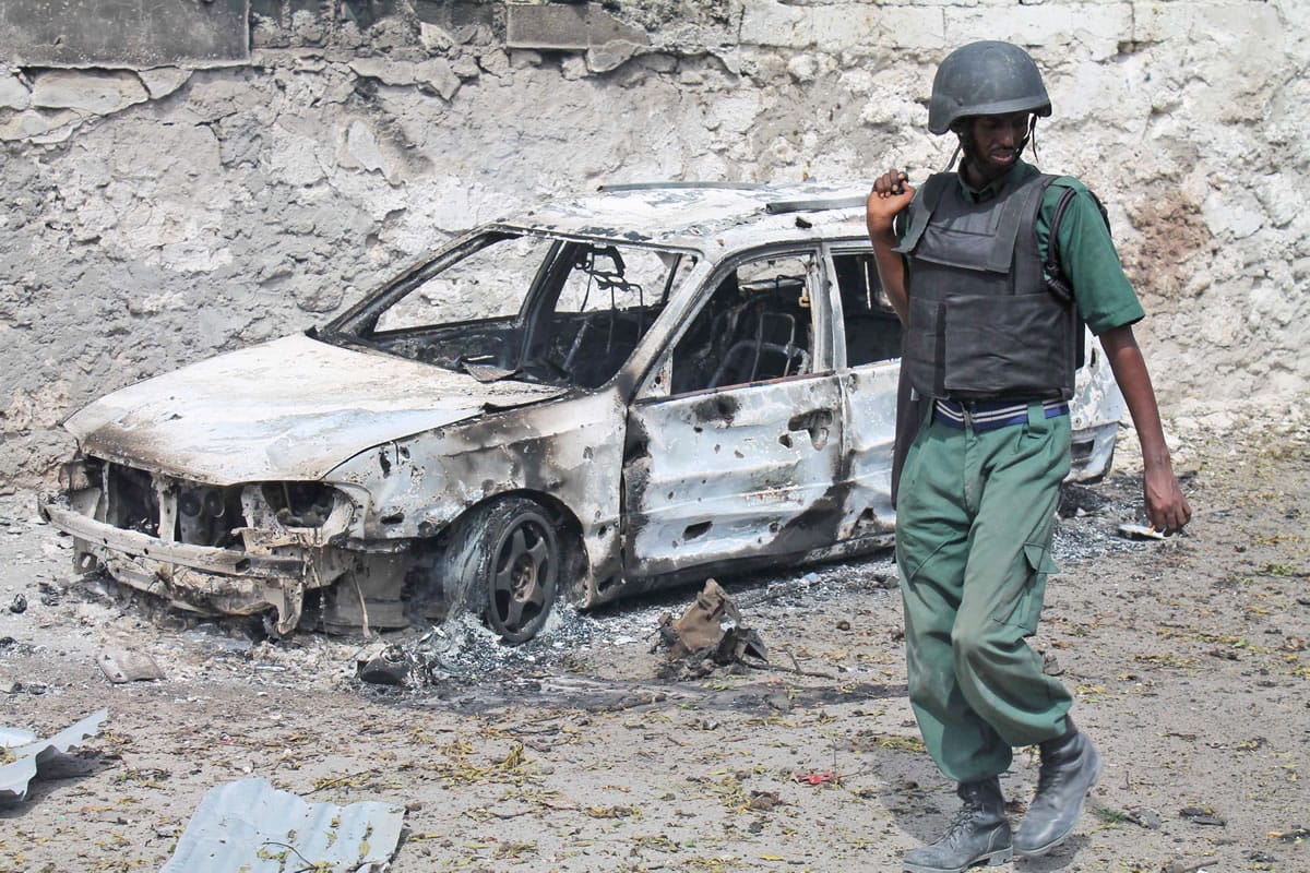 A Somali soldier walks near a destroyed car near the entrance of Mogadishu's court complex.