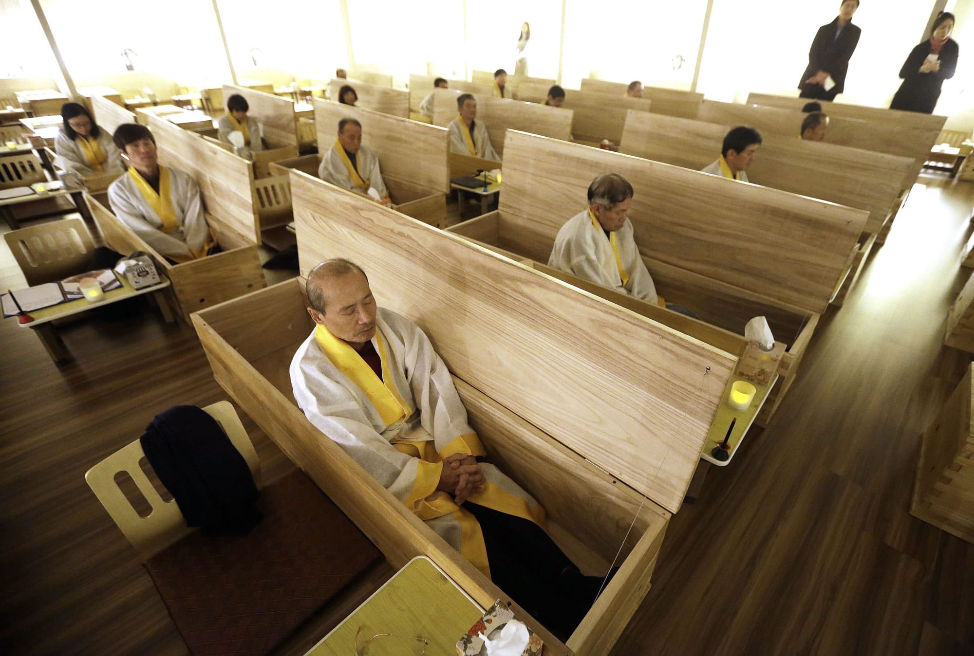 Wang Yong-yo, left bottom, sits inside a wooden coffin during the &quot;death experience&quot; program at Hyowon Healing Center in Seoul, South Korea, on Tuesday. In a dark, dimly-lit room, people dressed in white burial shrouds sit down next to dozens of coffins. They write their wills, climb into the caskets, lie down and a symbolic ?angel of death?