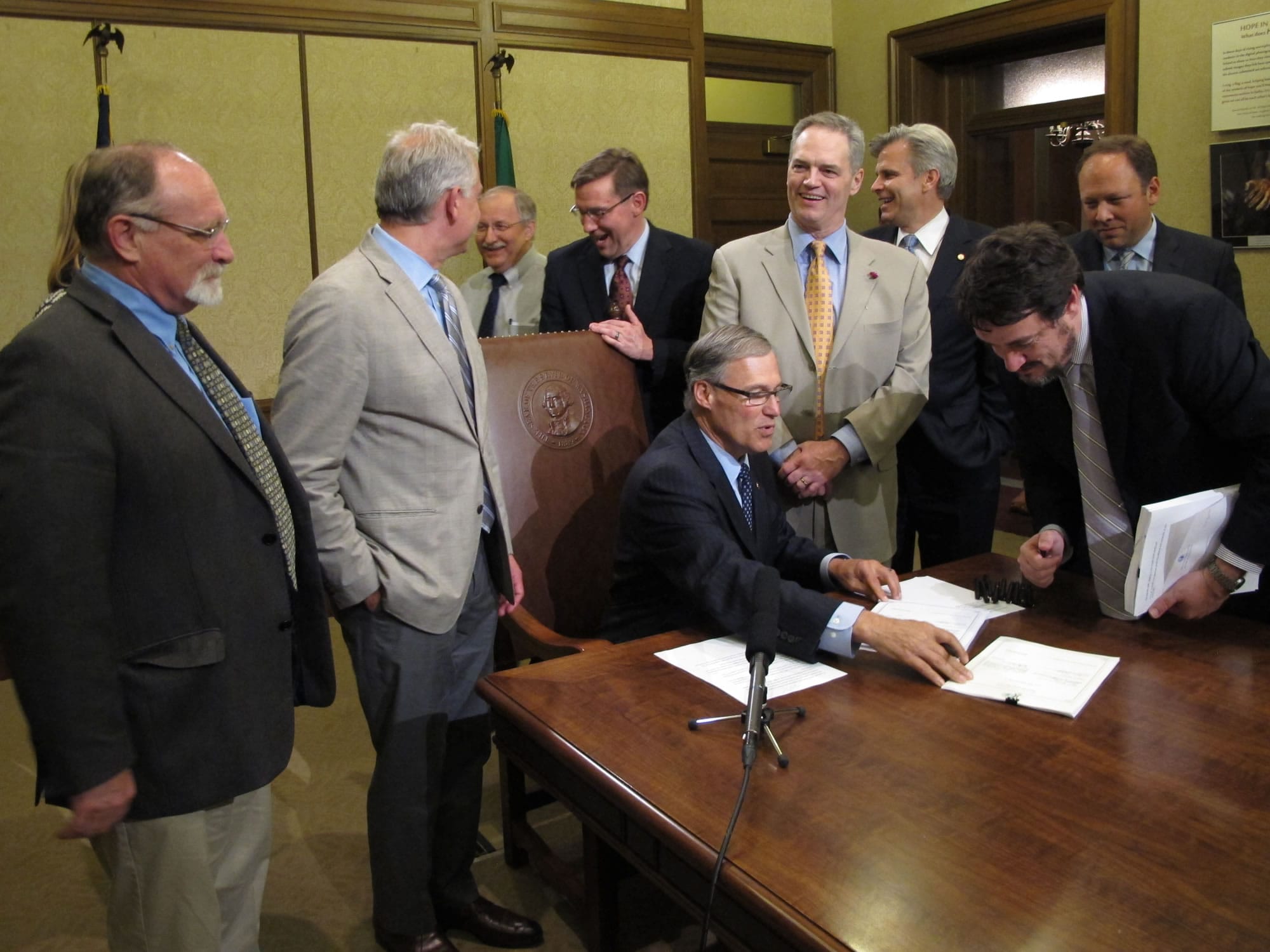 Gov. Jay Inslee, seated, is joined by several lawmakers as he prepares to sign a measure to make a legislative fix to the estate tax law, on Friday in Olympia.