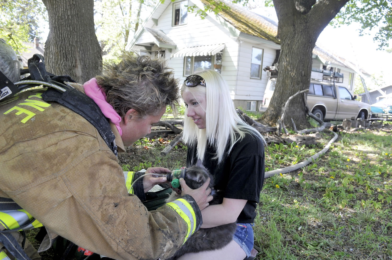 Firefighter Bridget Luby, left, holds an oxygen mask on Chief, a 10-year-old cat belonging to Haley Major, right, outside the heavily damaged house on Eighth Avenue near Napa Street in Spokane on Thursday.
