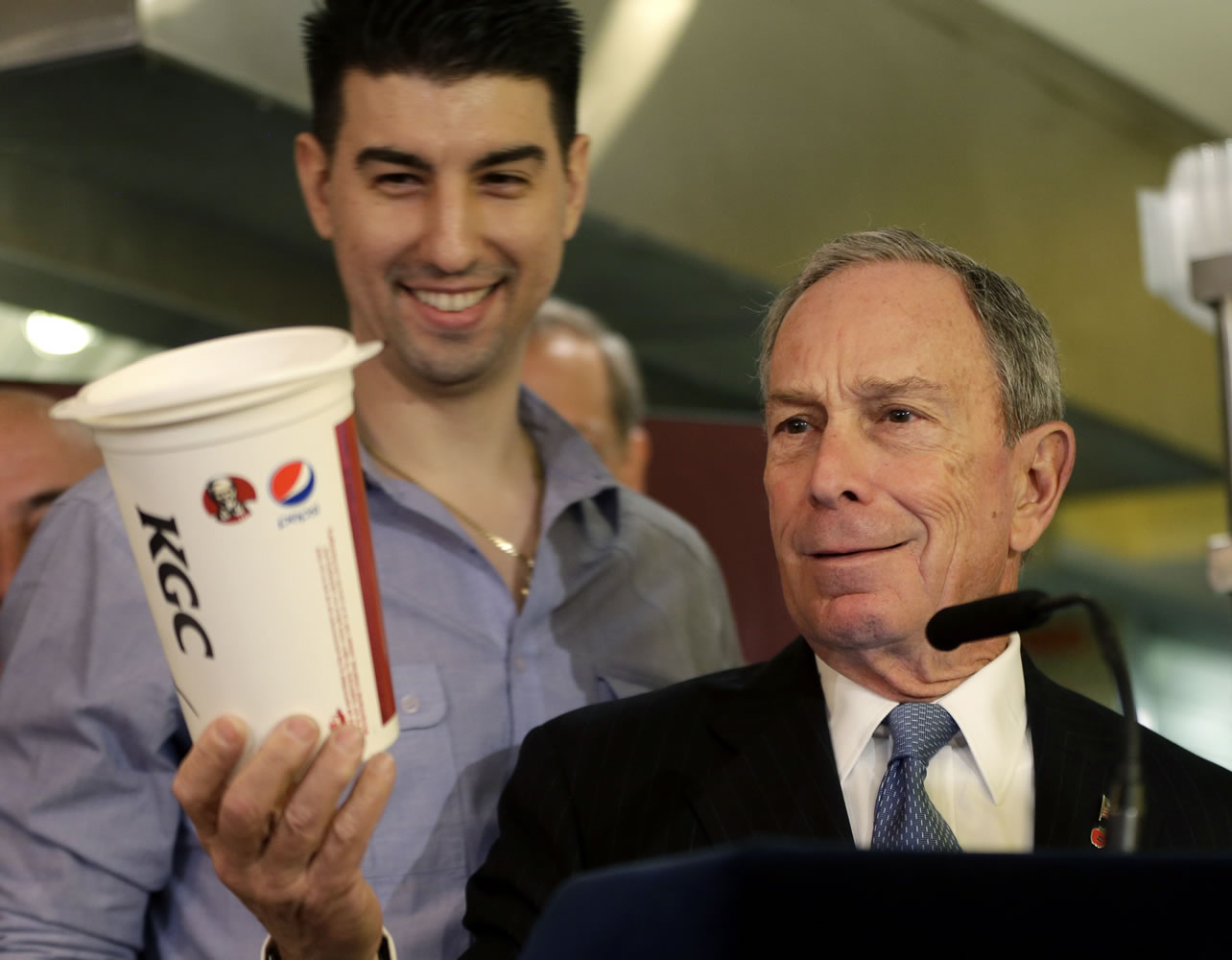 New York City Mayor Michael Bloomberg looks at a 64 ounce cup, with Lucky's Cafe owner Greg Anagnostopoulos, left, standing behind him, during a news conference at the cafe in New York on Tuesday.