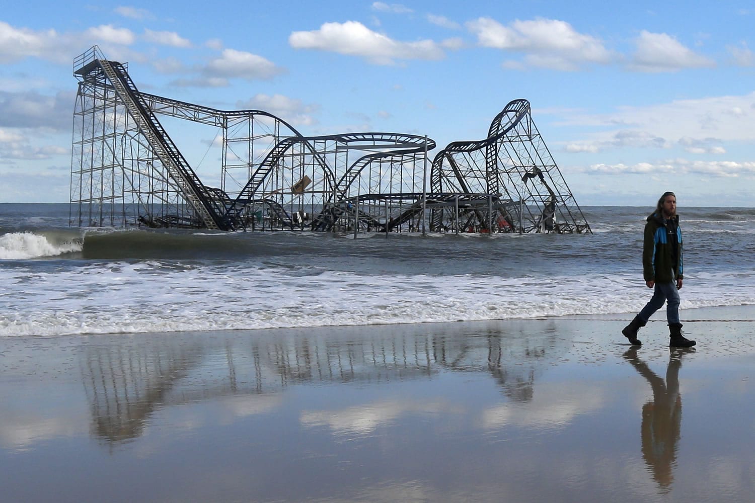 John Okeefe walks on the beach as a rollercoaster that once sat on the Funtown Pier in Seaside Heights, N.J., rests in the ocean on Wednesday, Oct.