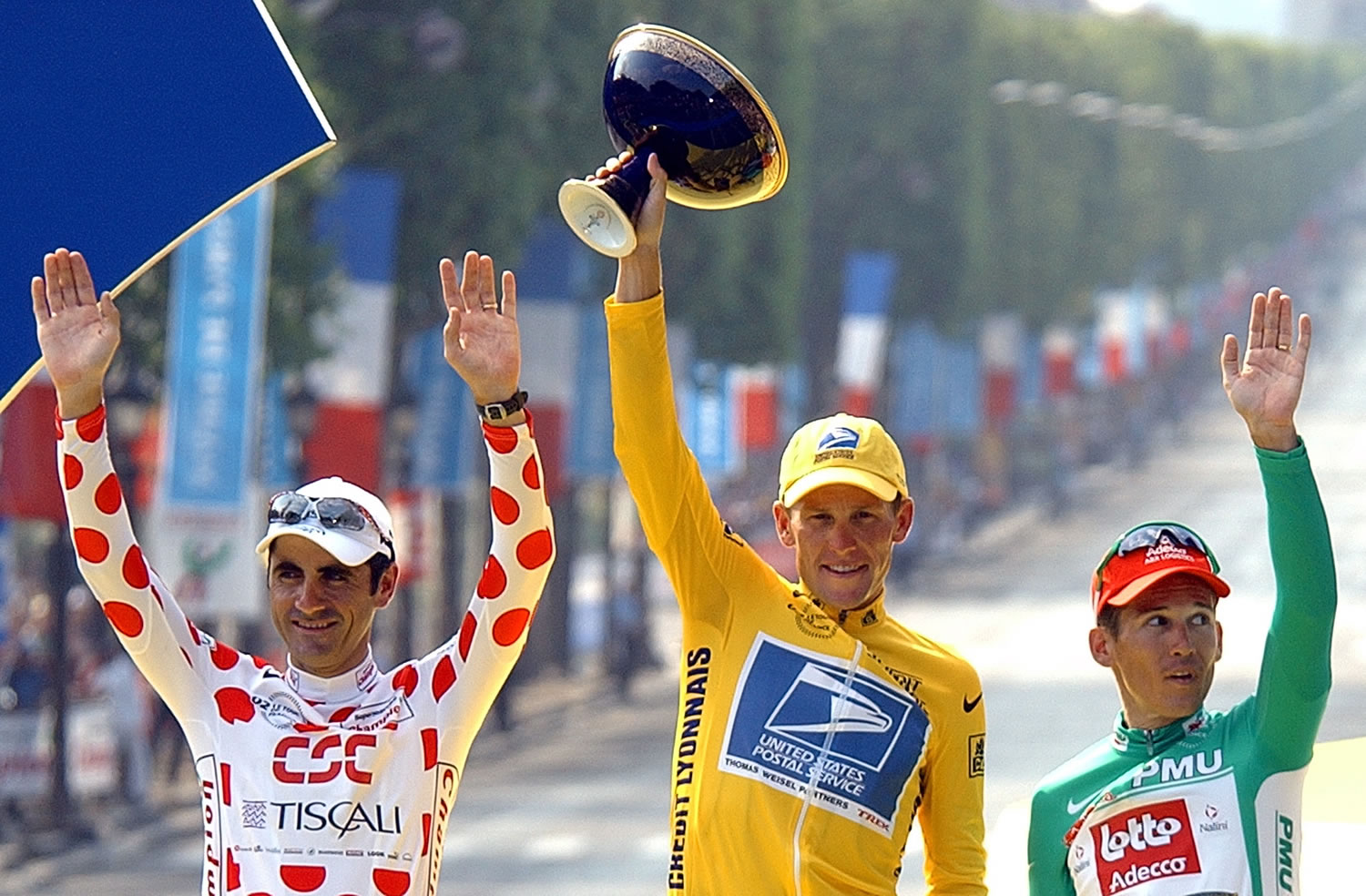Lance Armstrong, center, waving from the podium as he holds the winner's trophy July 28, 2002, along with best sprinter Robbie McEwen, of Australia, right, and best climber Laurent Jalabert, of France, after the 20th and final stage of the Tour de France cycling race between Melun and Paris.