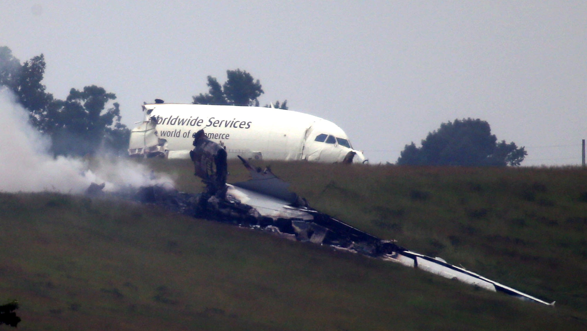 Debris burns as the broken fusilage of an A300 cargo plane lies on a hill at Birmingham-Shuttlesworth International Airport after crashing on approach Wednesday morning in Birmingham, Ala.