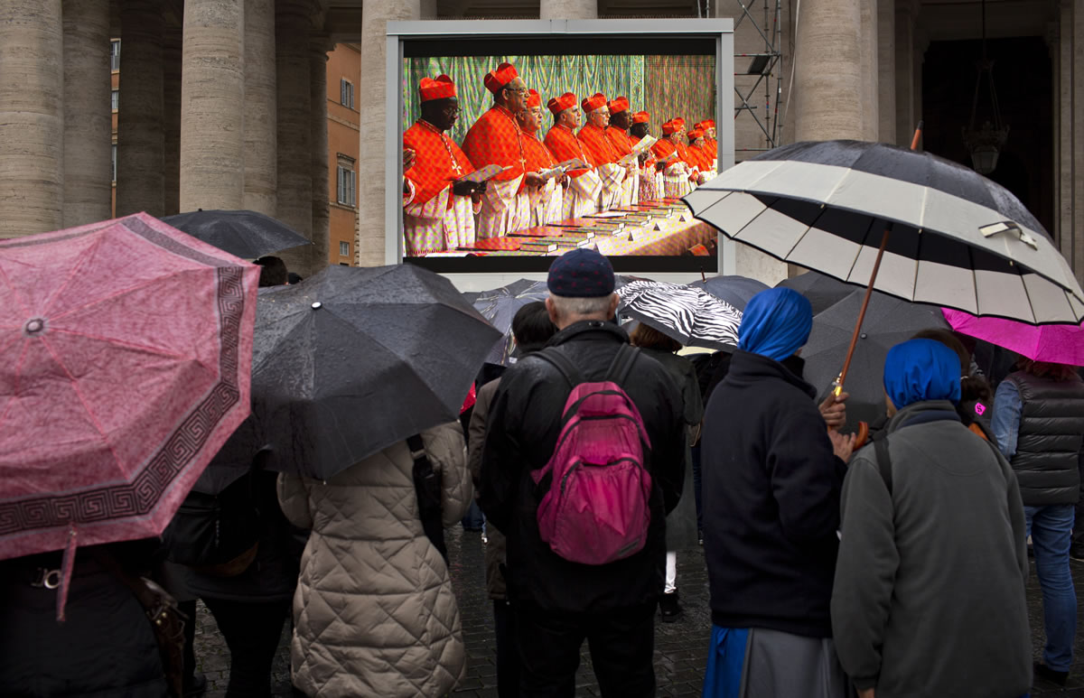 Faithful hold their umbrellas as they follow cardinals taking an oath inside the Sistine Chapel at the start the conclave on a video monitor in St.