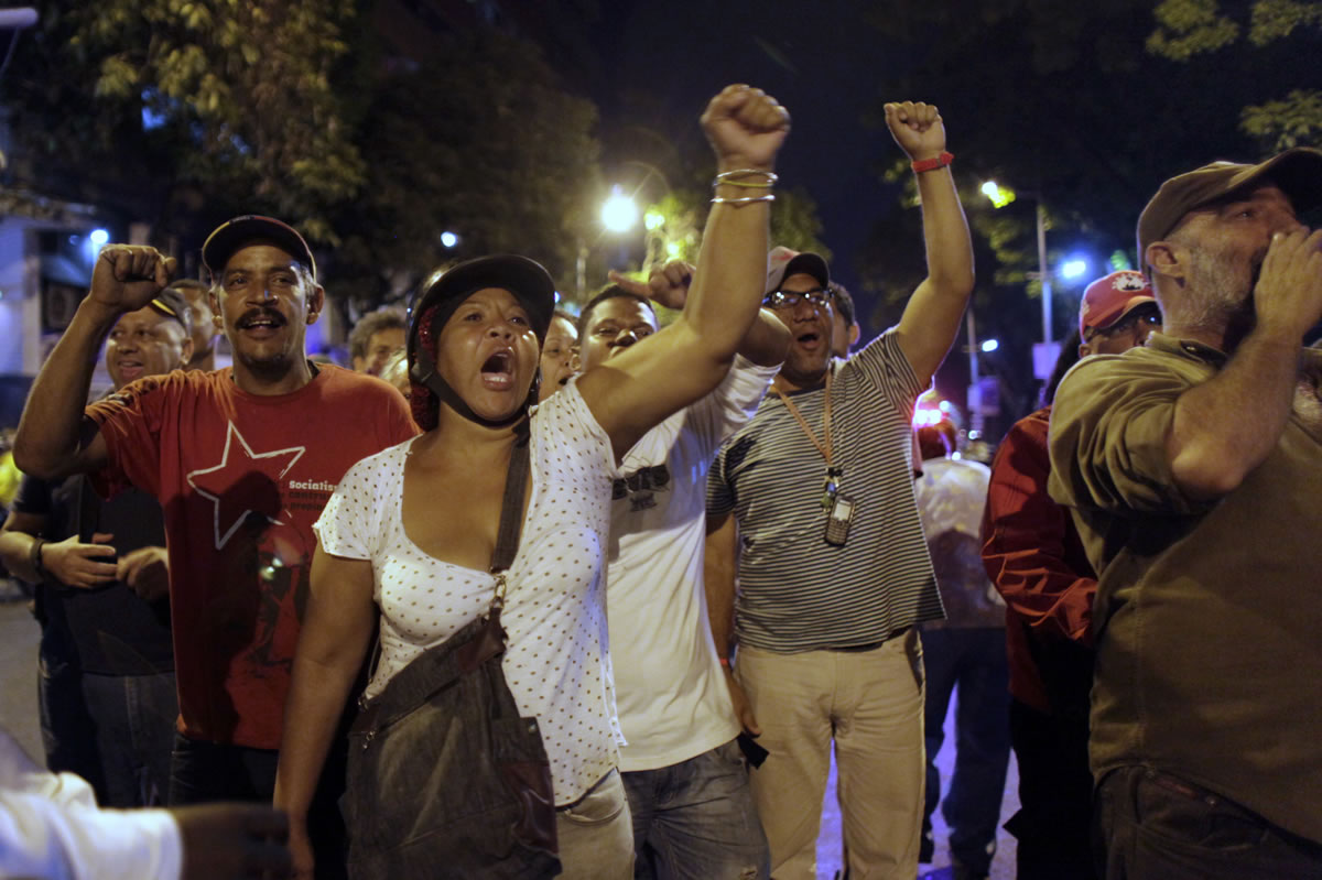 Government supporters chant slogans praising Venezuela's late President Hugo Chavez at opposition supporters, outside a a polling station Sunday, in Caracas, Venezuela.
