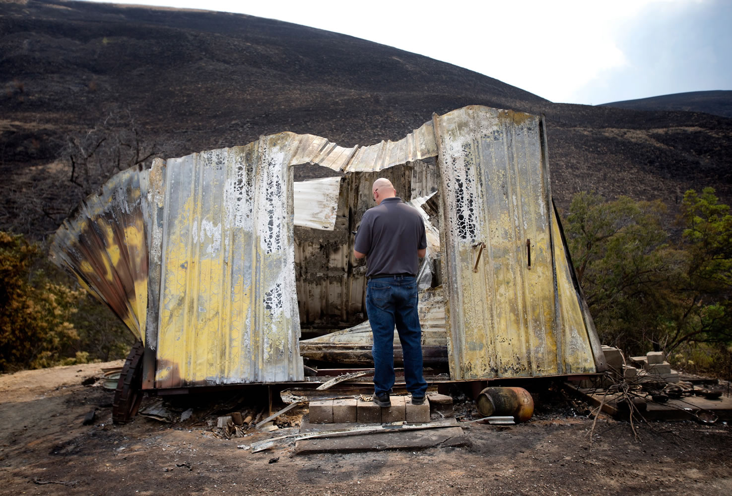Insurance adjuster Eric Nieuwenhuis looks over the remnants of a small outbuilding that held antiques that was destroyed in the Colockum Tarps Fire near Don Keeley's home Wednesday south of Malaga.