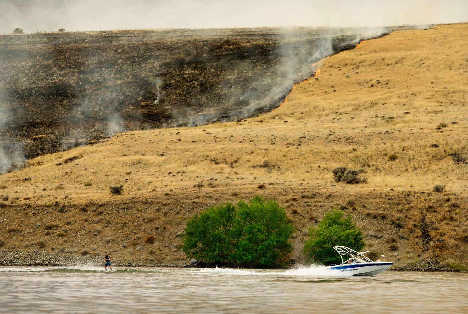 A wakeboarder cruises past a line of fire from the Colockum Tarps Fire along the Columbia River on Monday afternoon near the Crescent Bar Golf Course south of Malaga.