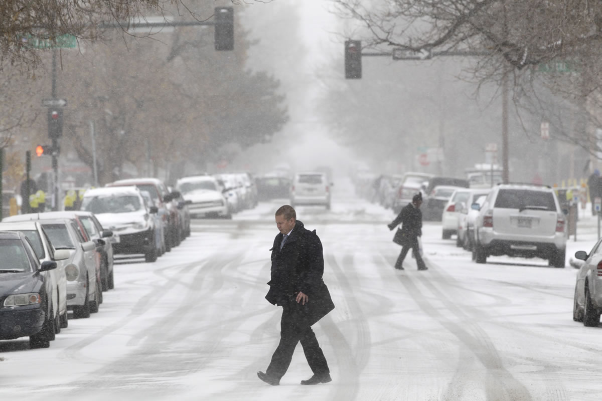 A man crosses the street during a winter storm that brought some snow and a fast plunge in temperature overnight to downtown Denver on Tuesday.