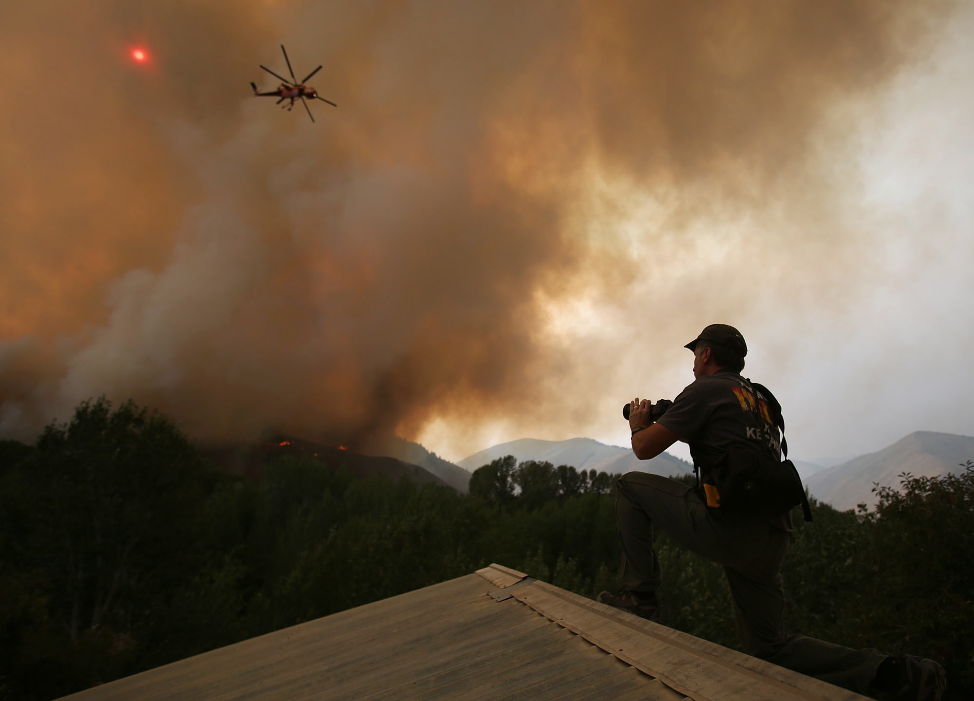 John Koth, photographs helicopters from the roof of a neighbors home while they battle the 64,000 acre Beaver Creek Fire on Friday north of Hailey, Idaho.