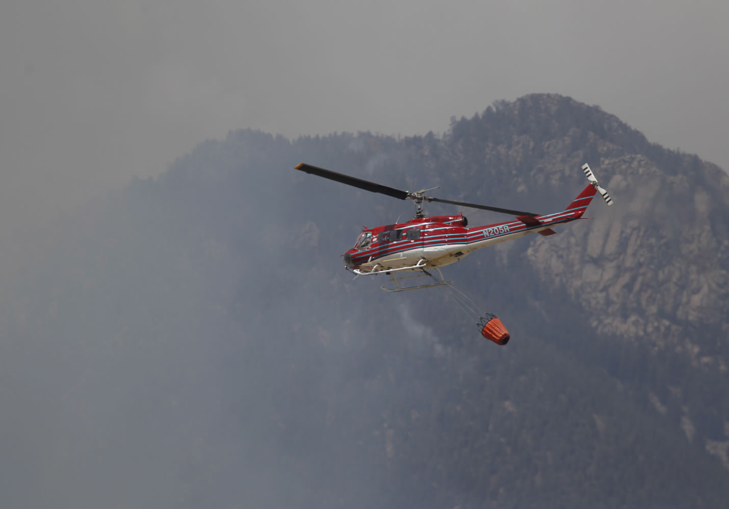 Bucket in tow, a helicopter makes a run as a wildfire rolls through housing subdivisions in the mountains north and west of Colorado Springs, Colo., on Wednesday, June 27, 2012. The fire has forced the evacuation of more than 32,000 residents of the communities west of and now in Colorado Springs proper.