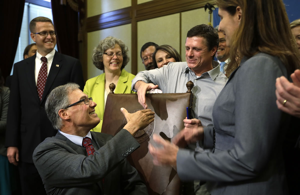 Gov. Jay Inslee, seated left, turns to shake hands with Alan Northrop, a former Clark County resident, after Inslee signed into law a measure that would allow people who have been wrongfully convicted to seek state compensation for the years they were imprisoned on Wednesday in Olympia.