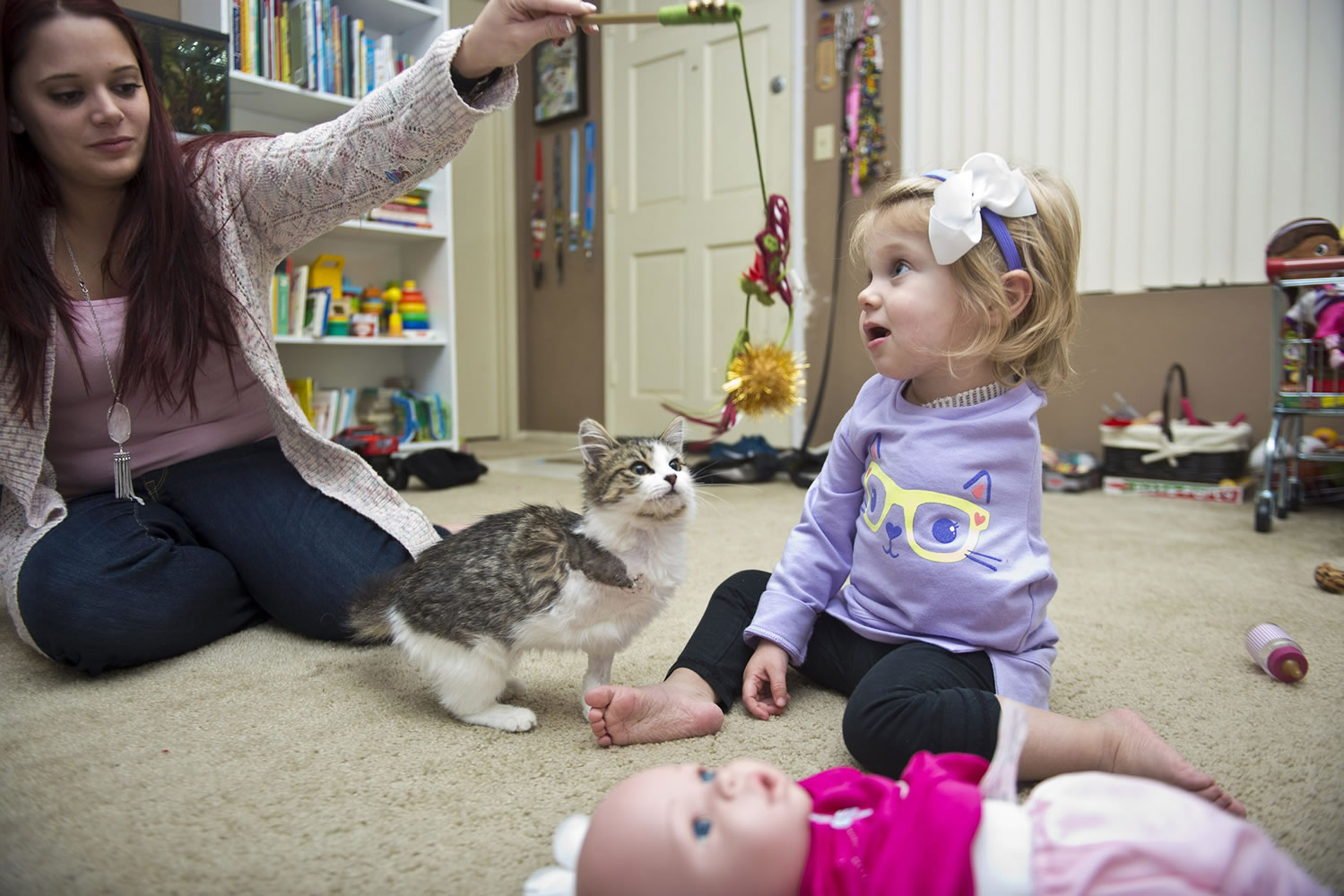 Simone Tipton, left, dangles a cat toy as she and daughter Scarlette, 2, play with their new kitten, Doc. Tipton and husband Matt searched for six months to find an amputee cat for their daughter, who had an arm amputated during a battle with cancer.