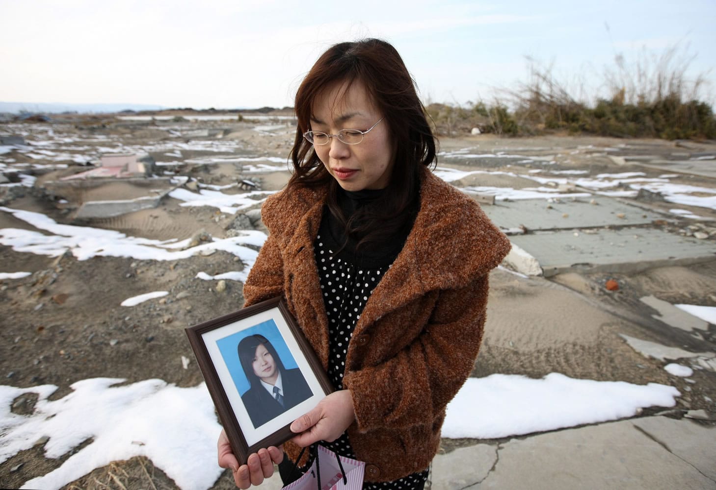 Yukari Abe holds a photo of her daughter Chikako at the site where her family's home stood before the March 11, 2011 earthquake and tsunami in Minamisoma, Japan.