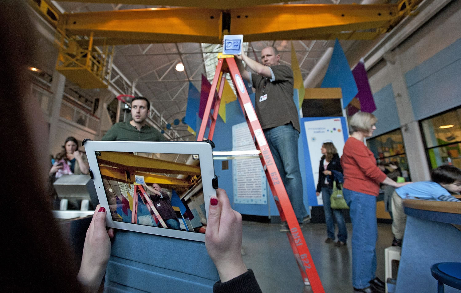 Washington State University Vancouver student Madi Kozacek, foreground left, points an iPad at an object representing the digital hot spots that will be installed on a display automobile at the Oregon Museum of Science and Industry in Portland. OMSI's Jeff Varner, center, holds the object at the appropriate height. At right is WSUV student Jason Clark.