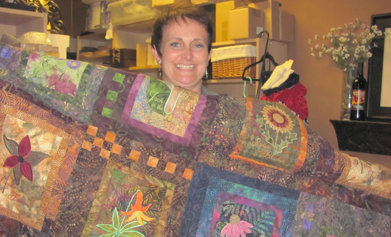 Carrie Schulstad shows off one of the many intricate quilts currently filling the back room of her store, The Uncommon Gift.