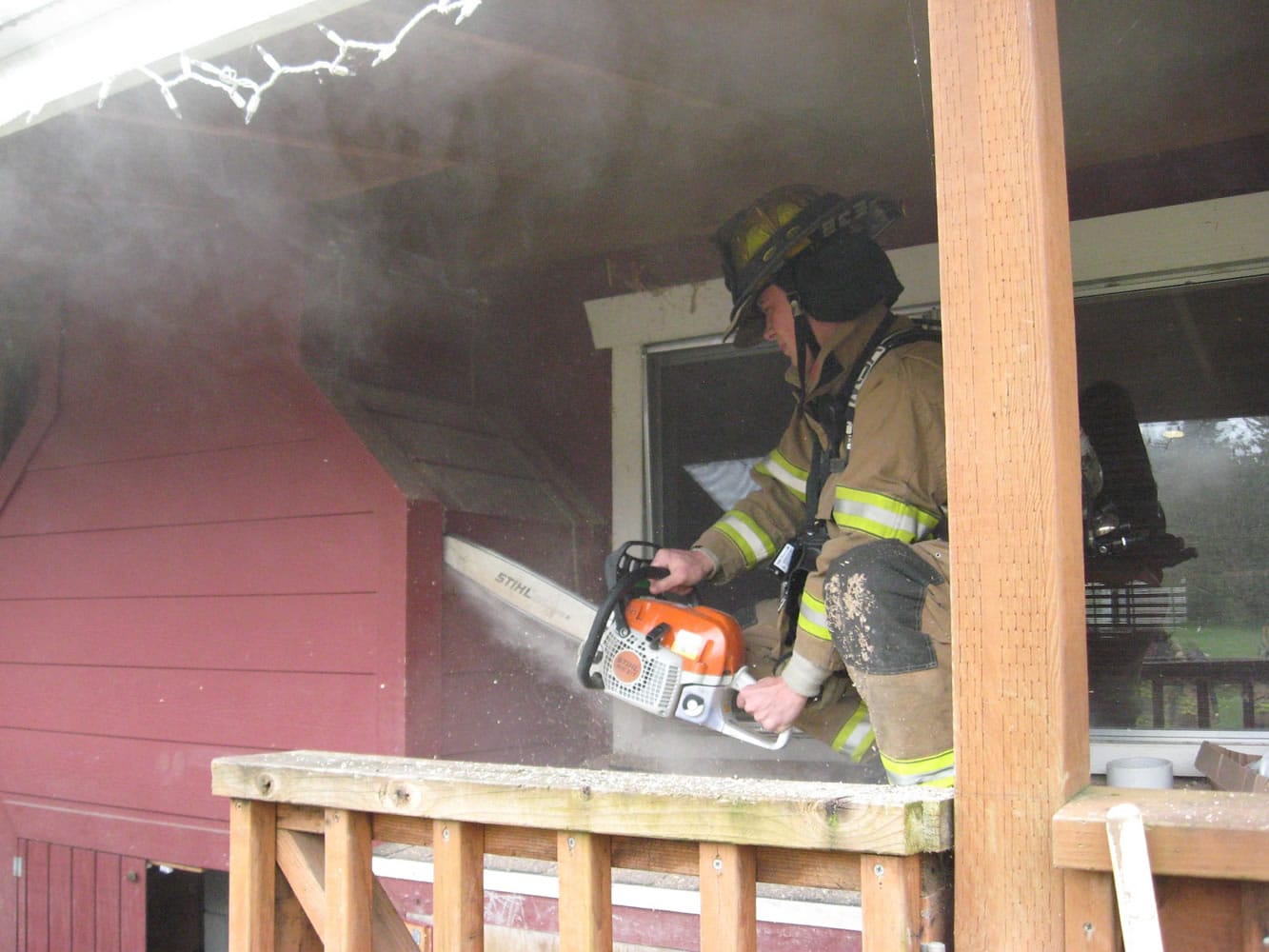 Firefighter Brian George cuts into the outside of a home where a wood stove insert and wood framing around it caught fire on Wednesday afternoon.
