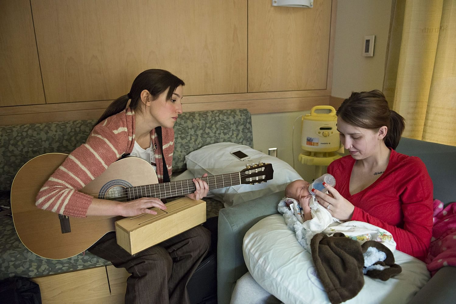 Music therapist Susan Palmieri, left, taps on a Gato box instrument as Haley Giese feeds her newborn son, Miles, a bottle Tuesday afternoon in PeaceHealth Southwest Medical Center&#039;s neonatal intensive care unit. Palmieri uses the Gato box to help Miles pace his sucking while feeding.