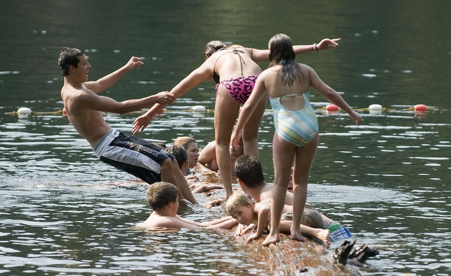 Swimmers determine who has the best balance on a floating log in the lake's swimming area.